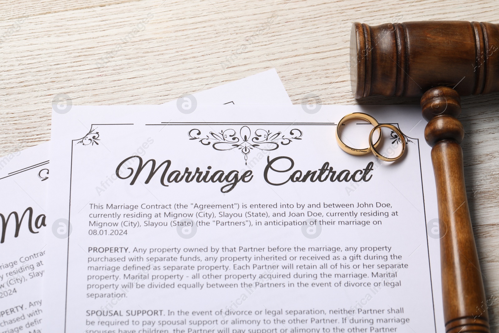 Photo of Marriage contract, golden wedding rings and gavel on wooden table