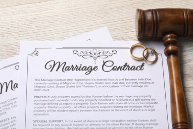 Photo of Marriage contract, golden wedding rings and gavel on wooden table