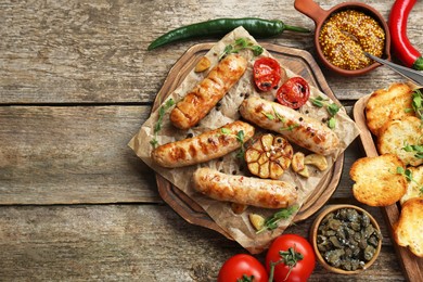 Tasty fresh grilled sausages with vegetables on wooden table, flat lay. Space for text