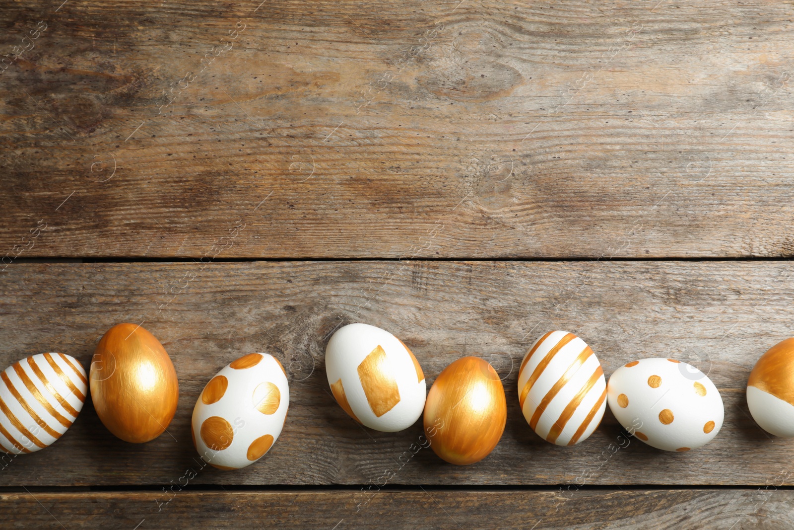 Photo of Set of traditional Easter eggs decorated with golden paint on wooden background, top view. Space for text