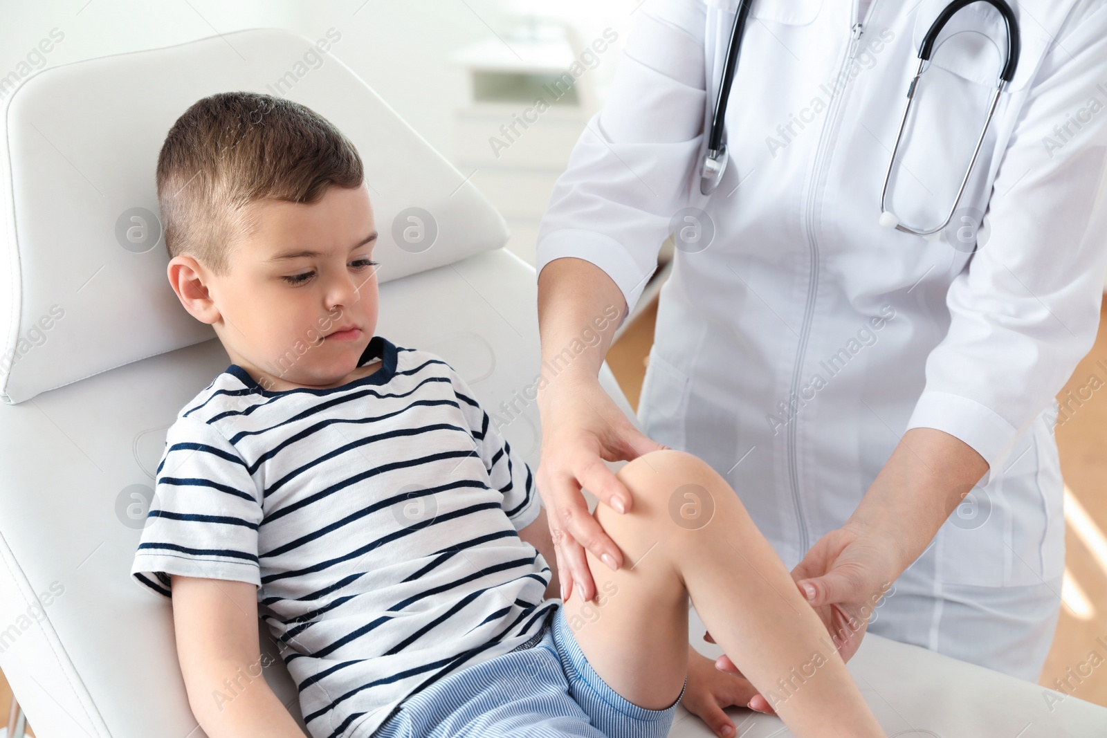 Photo of Doctor examining little patient with knee problems in clinic