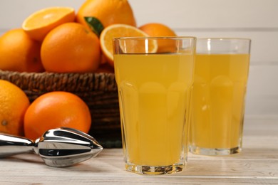 Photo of Many ripe juicy oranges, squeezer and fresh juice on white wooden table