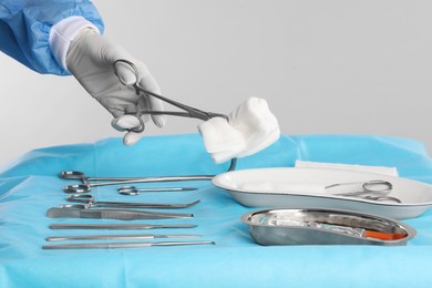 Photo of Doctor holding forceps with tissue over surgical instruments on table against light background, closeup
