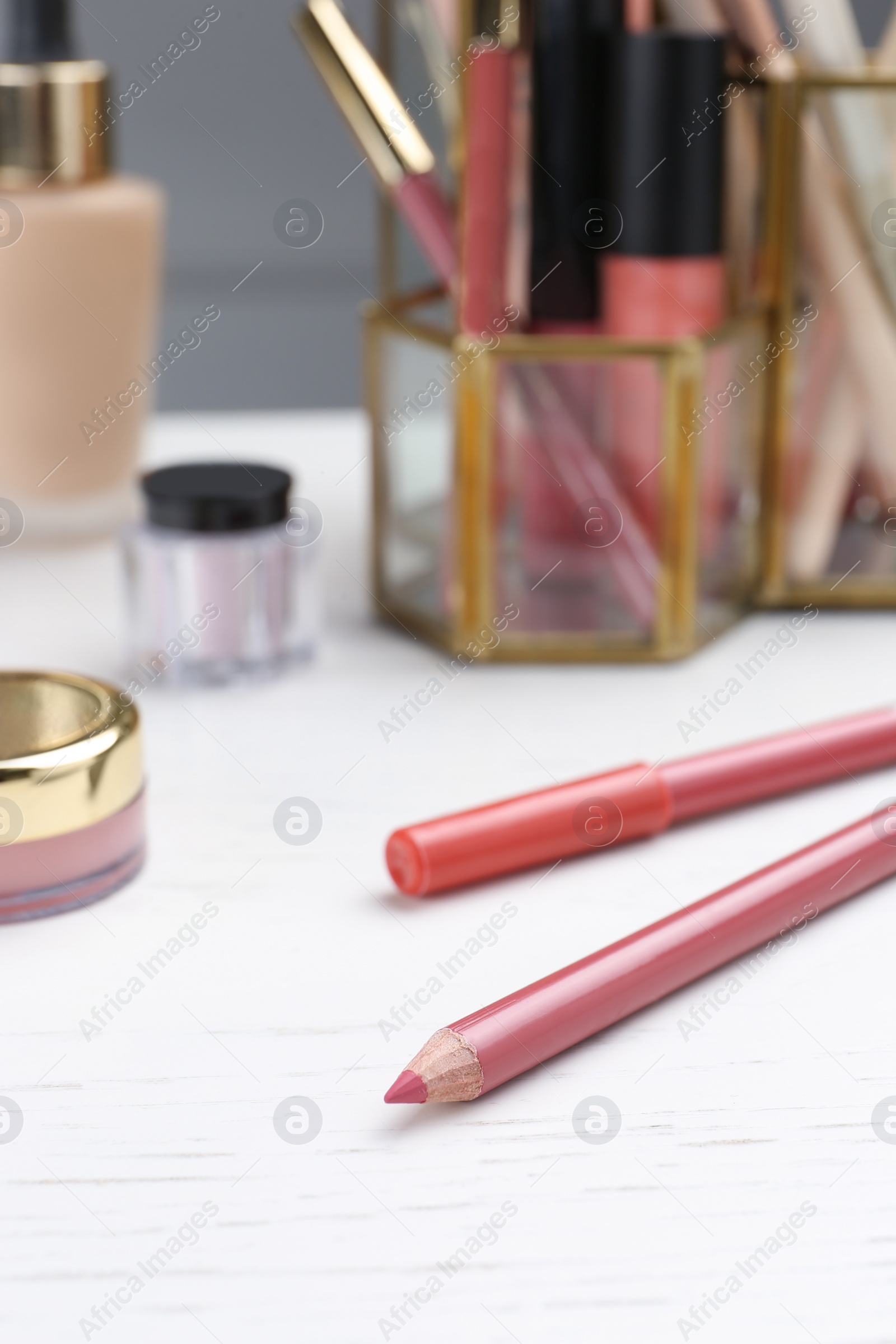 Photo of Lip pencils and other cosmetic products on white wooden table