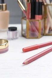 Lip pencils and other cosmetic products on white wooden table