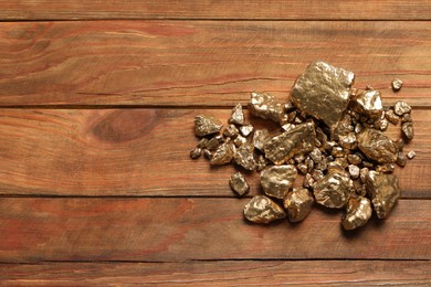 Photo of Pile of shiny gold nuggets on wooden table, flat lay. Space for text