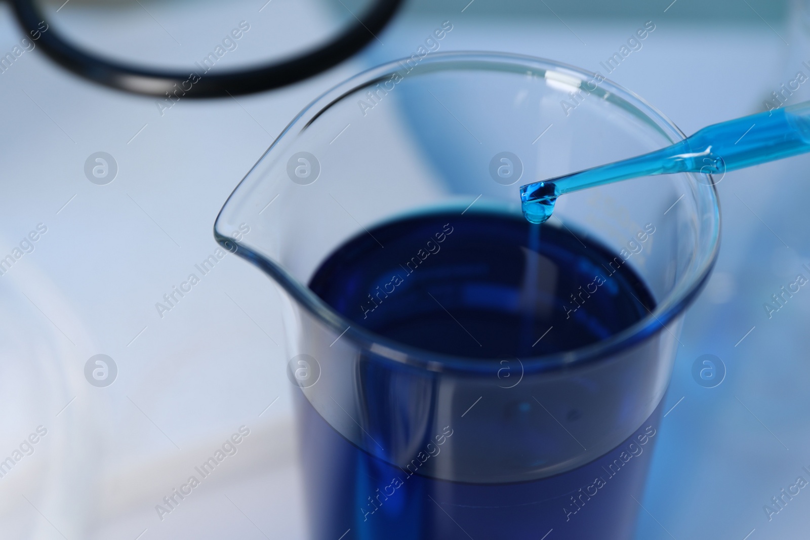 Photo of Laboratory analysis. Dripping blue liquid into beaker on white table, closeup