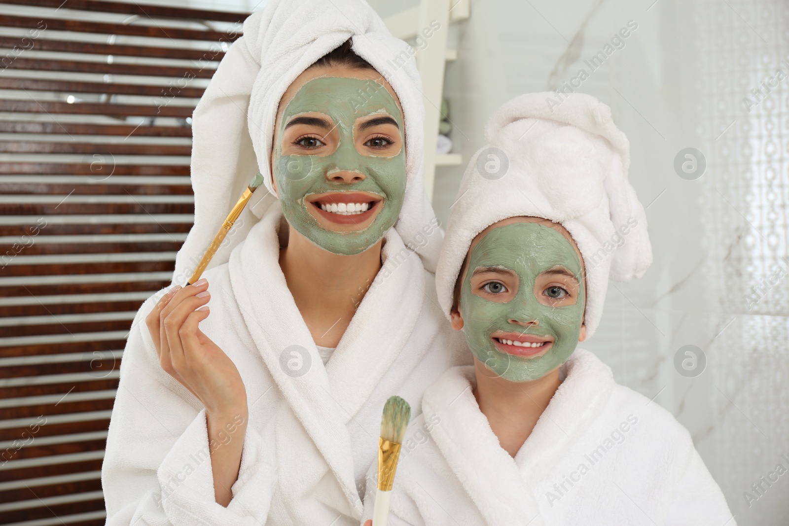 Photo of Young mother and her daughter with facial masks in bathroom