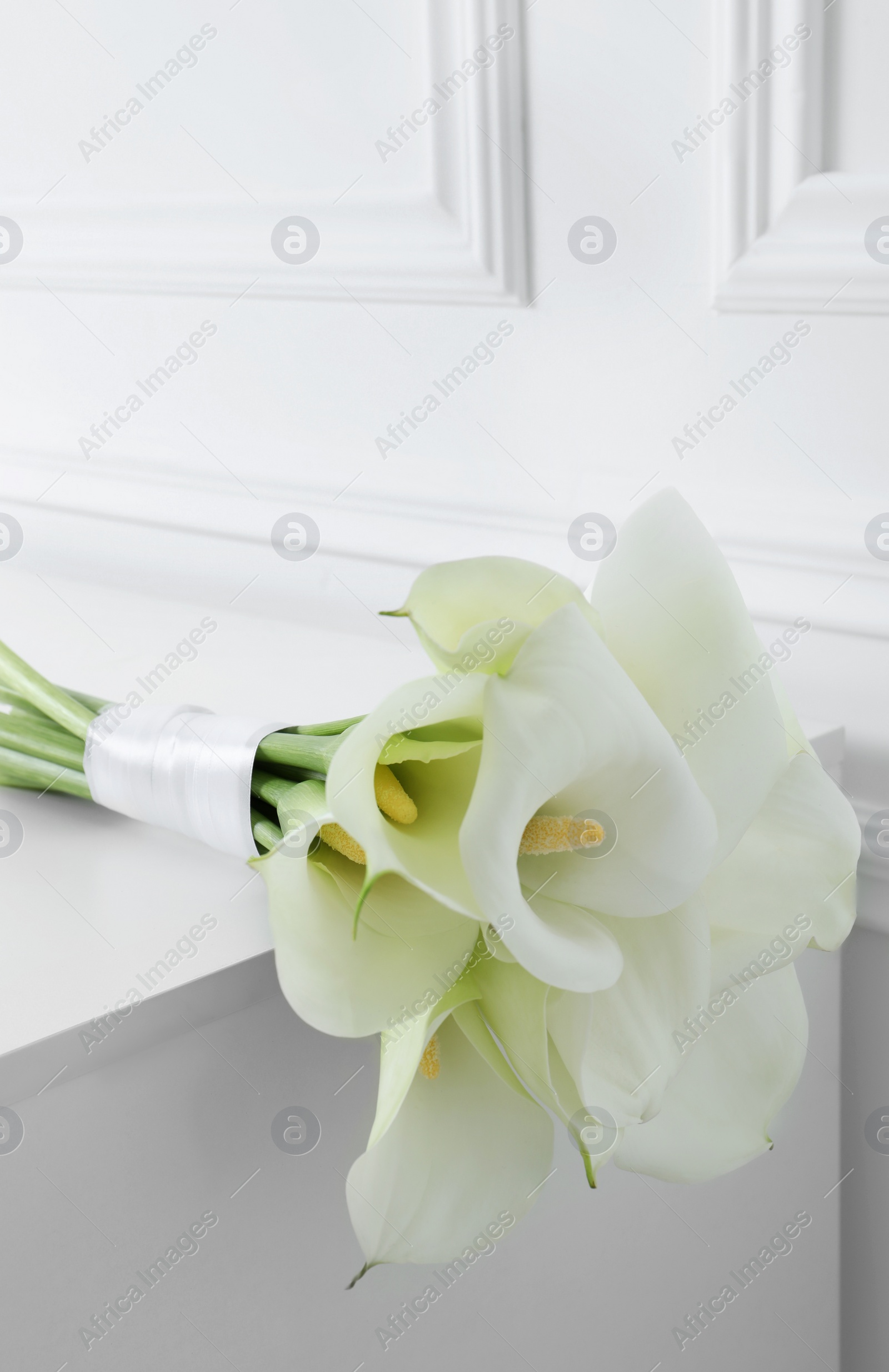 Photo of Beautiful calla lily flowers tied with ribbon on white table