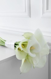 Photo of Beautiful calla lily flowers tied with ribbon on white table