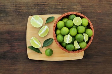 Photo of Whole and cut fresh ripe limes in bowl on wooden table, top view