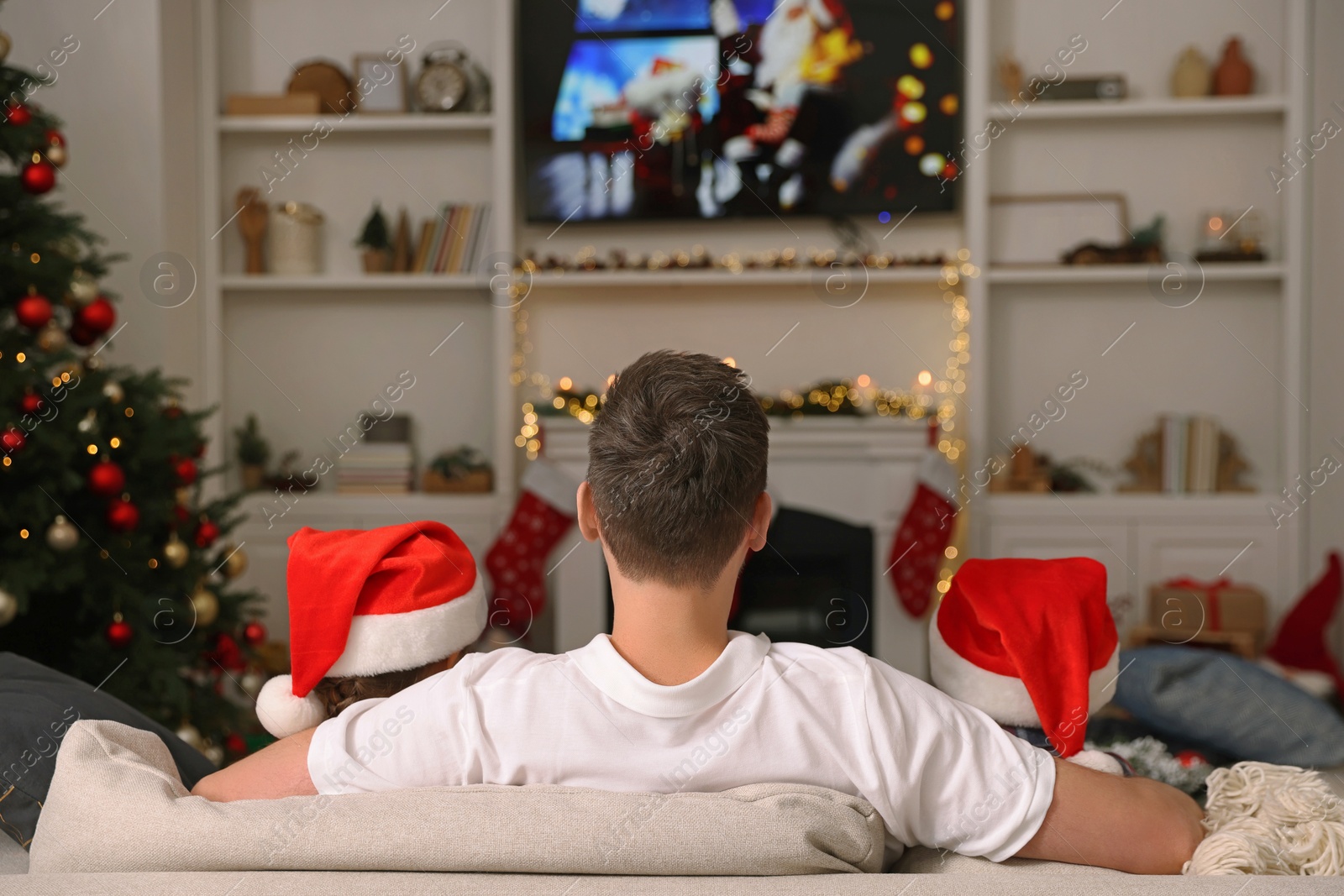 Photo of Father with his children watching TV in cosy room, back view. Christmas atmosphere