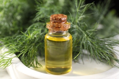 Bottle of essential oil and fresh dill on light tray, closeup