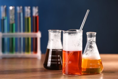 Photo of Laboratory glassware with colorful liquids on wooden table, space for text. Chemical reaction