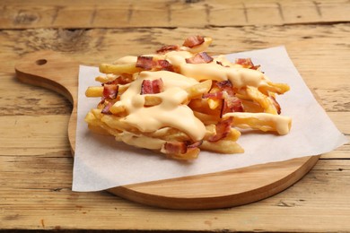 Delicious French fries with bacon and cheese sauce on wooden table, closeup