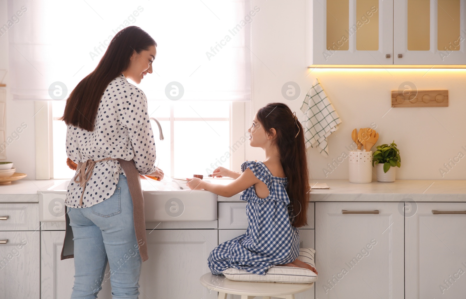 Photo of Mother and daughter washing dishes together in kitchen