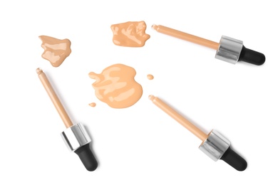 Photo of Samples of different foundation shades and droppers on white background, top view