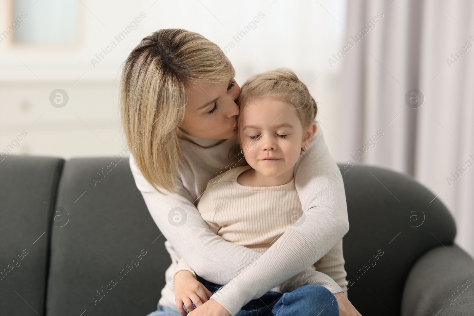 Photo of Mother kissing her daughter on sofa at home
