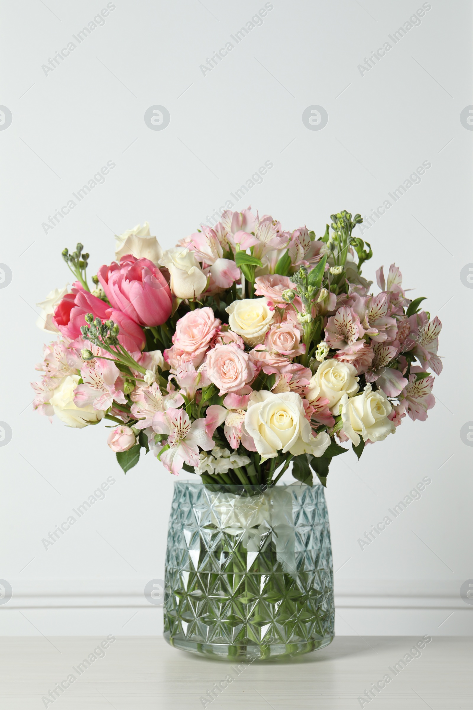 Photo of Beautiful bouquet of fresh flowers in vase on table near white wall