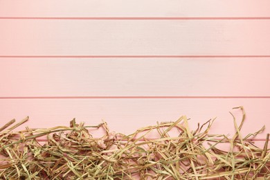 Heap of dried hay on pink wooden background, flat lay. Space for text