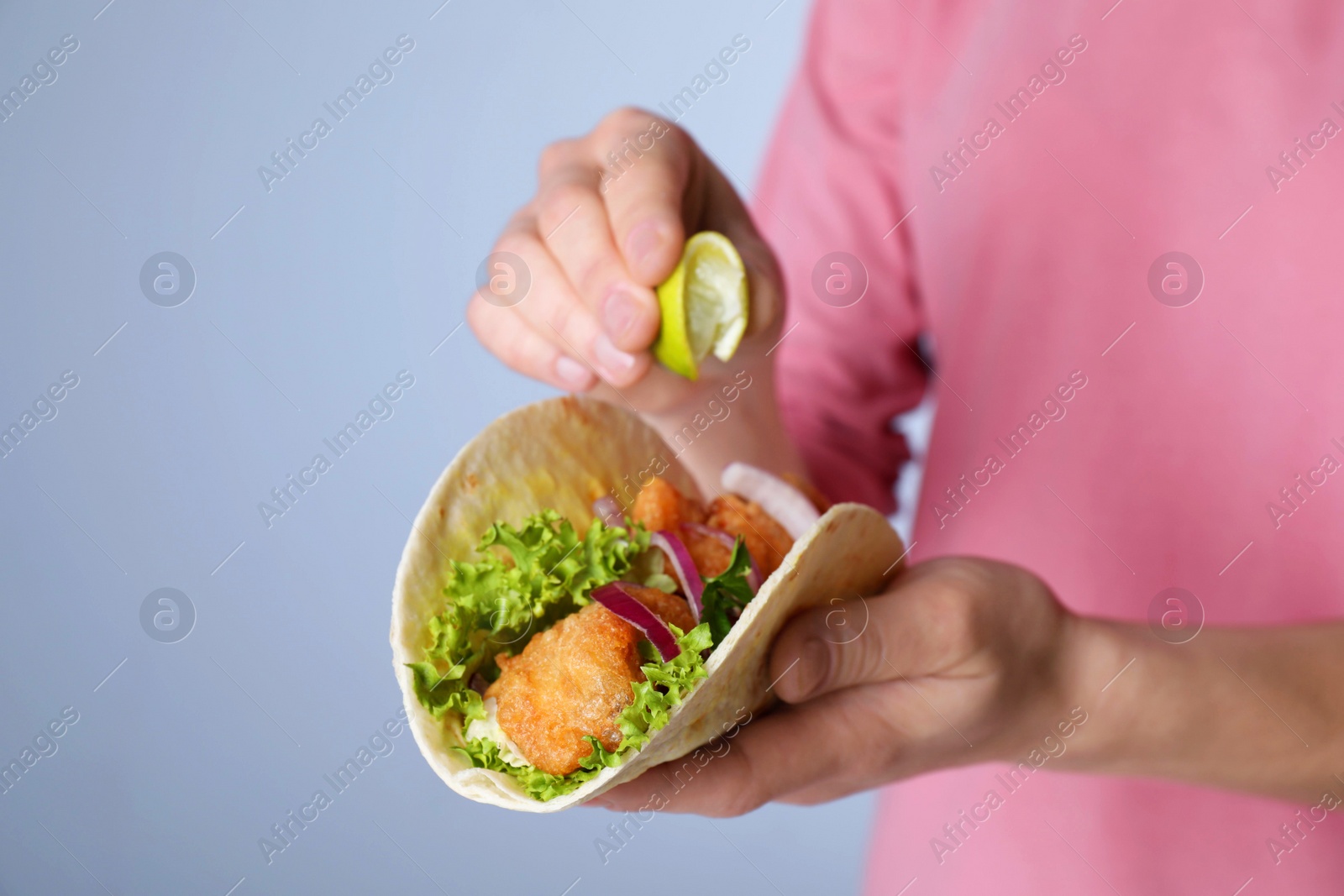 Photo of Woman squeezing lime on fish taco against grey background, closeup