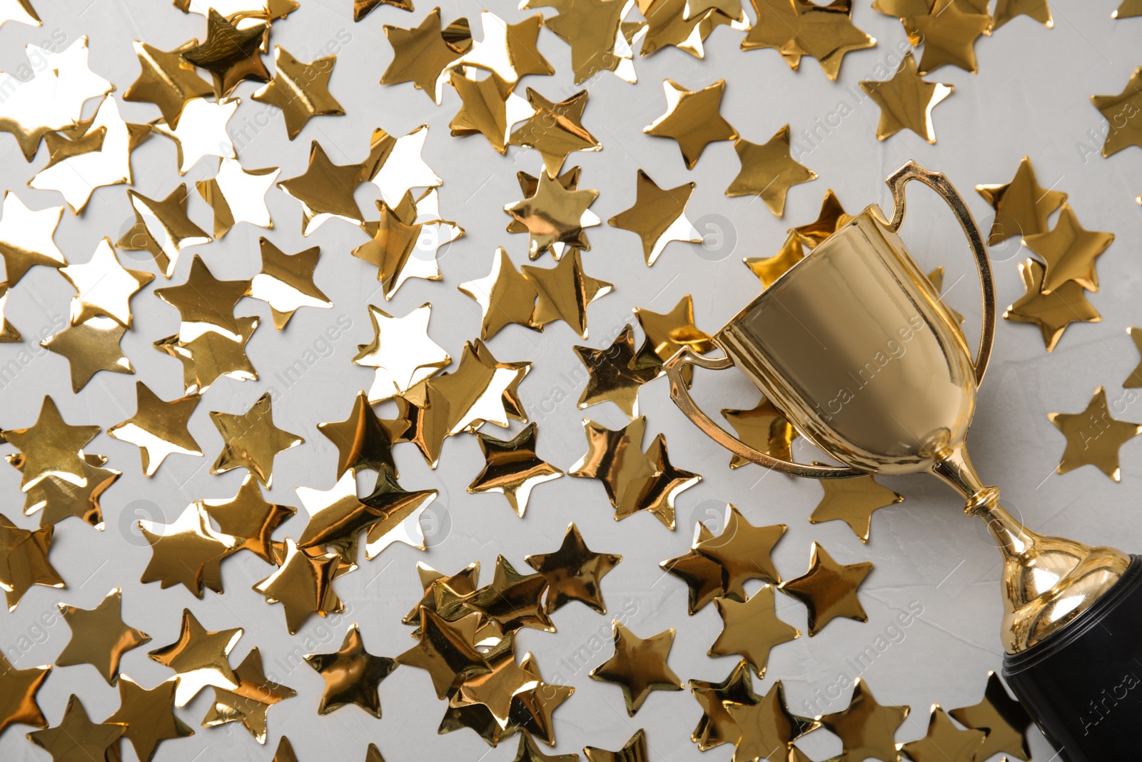 Photo of Gold trophy cup and confetti on light grey background, flat lay. Space for text