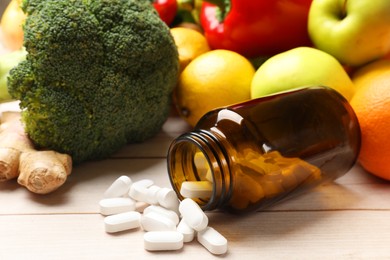 Photo of Dietary supplements. Overturned bottle with pills near food products on light wooden table, closeup