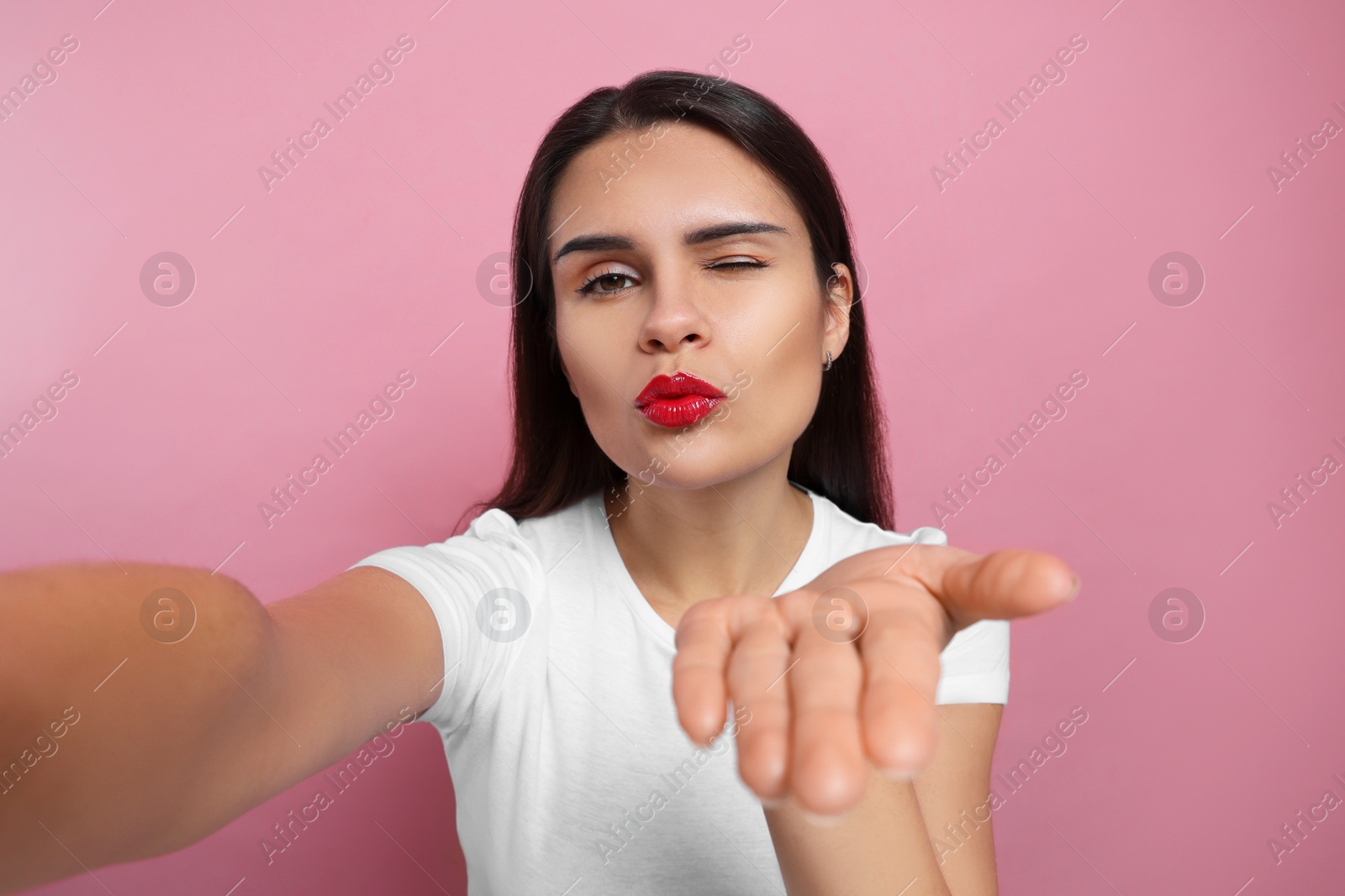 Photo of Beautiful young woman taking selfie while blowing kiss on pink background, closeup