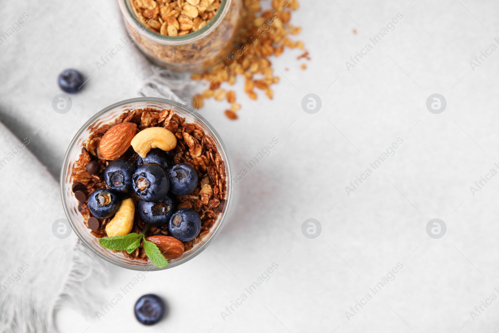 Photo of Tasty granola with berries, nuts and mint in glass on light table, top view. Space for text