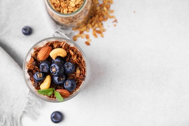 Photo of Tasty granola with berries, nuts and mint in glass on light table, top view. Space for text