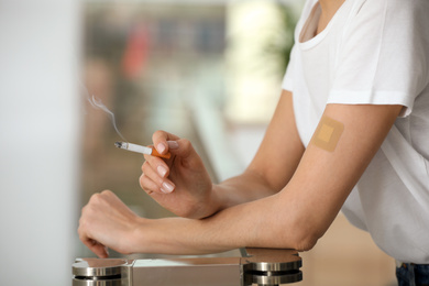 Photo of Young woman with nicotine patch and cigarette indoors, closeup