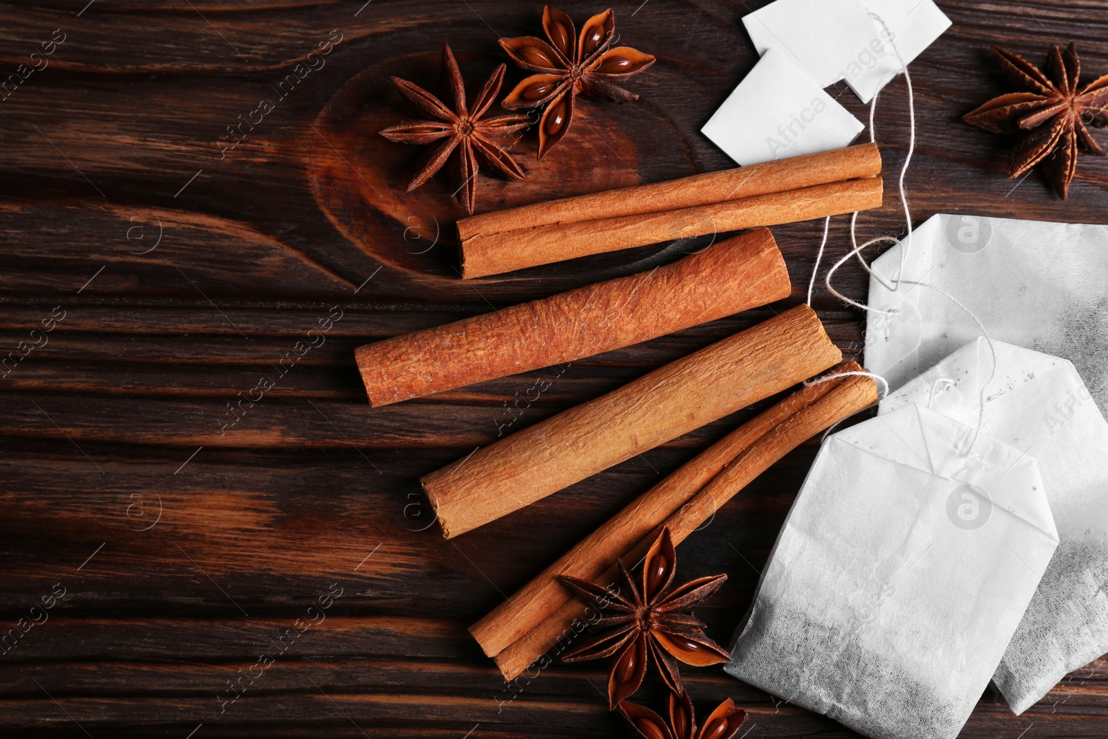 Photo of Tea bags, cinnamon sticks and anise stars on wooden table, flat lay. Space for text