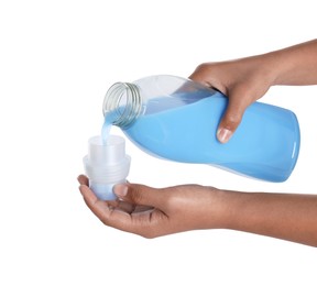 Photo of Woman pouring fabric softener from bottle into cap on white background, closeup