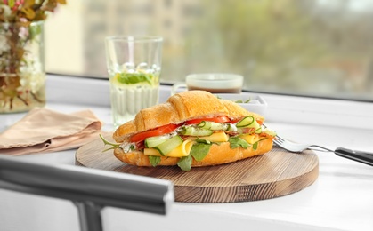 Photo of Tasty croissant sandwich with salami on window sill