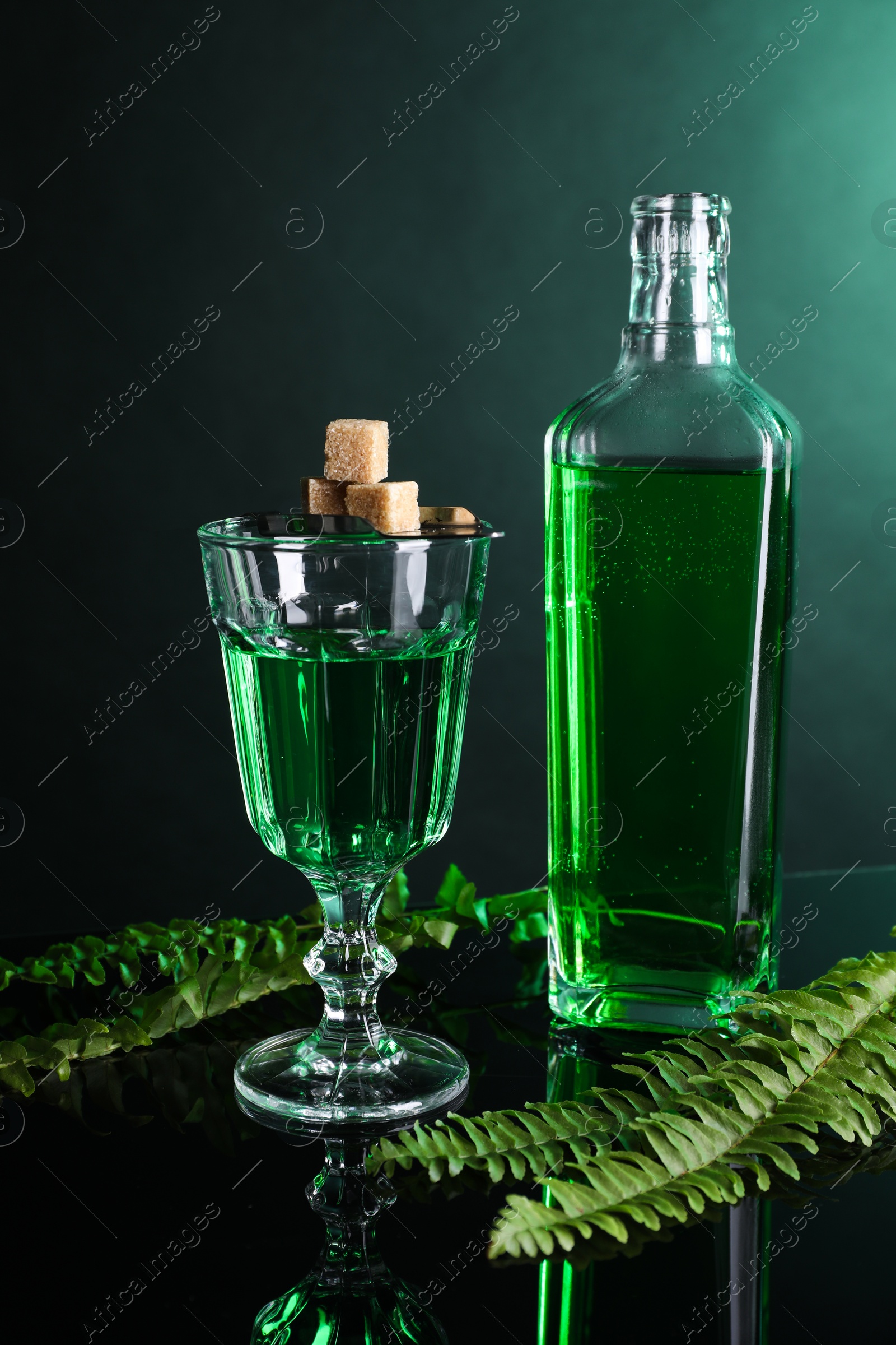 Photo of Absinthe, brown sugar and green leaves on mirror table. Alcoholic drink
