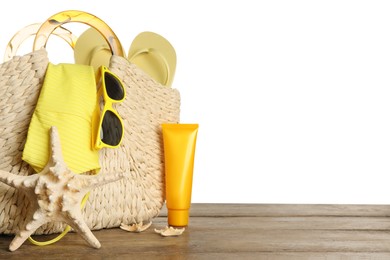 Bag with different beach objects on wooden table against white background