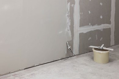 Photo of Bucket with putty knife near plastered wall indoors