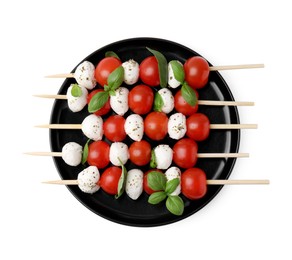 Photo of Plate of skewers with tomatoes, mozzarella balls, basil and spices isolated on white, top view