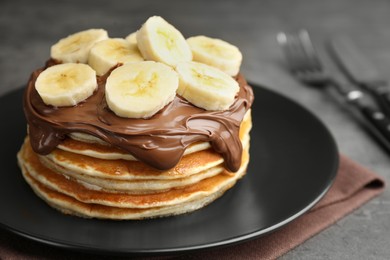 Photo of Tasty pancakes with chocolate spread and sliced banana on table, closeup