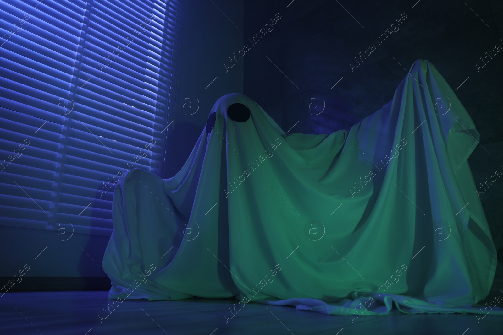 Photo of Creepy ghost. Woman covered with sheet near window in blue light