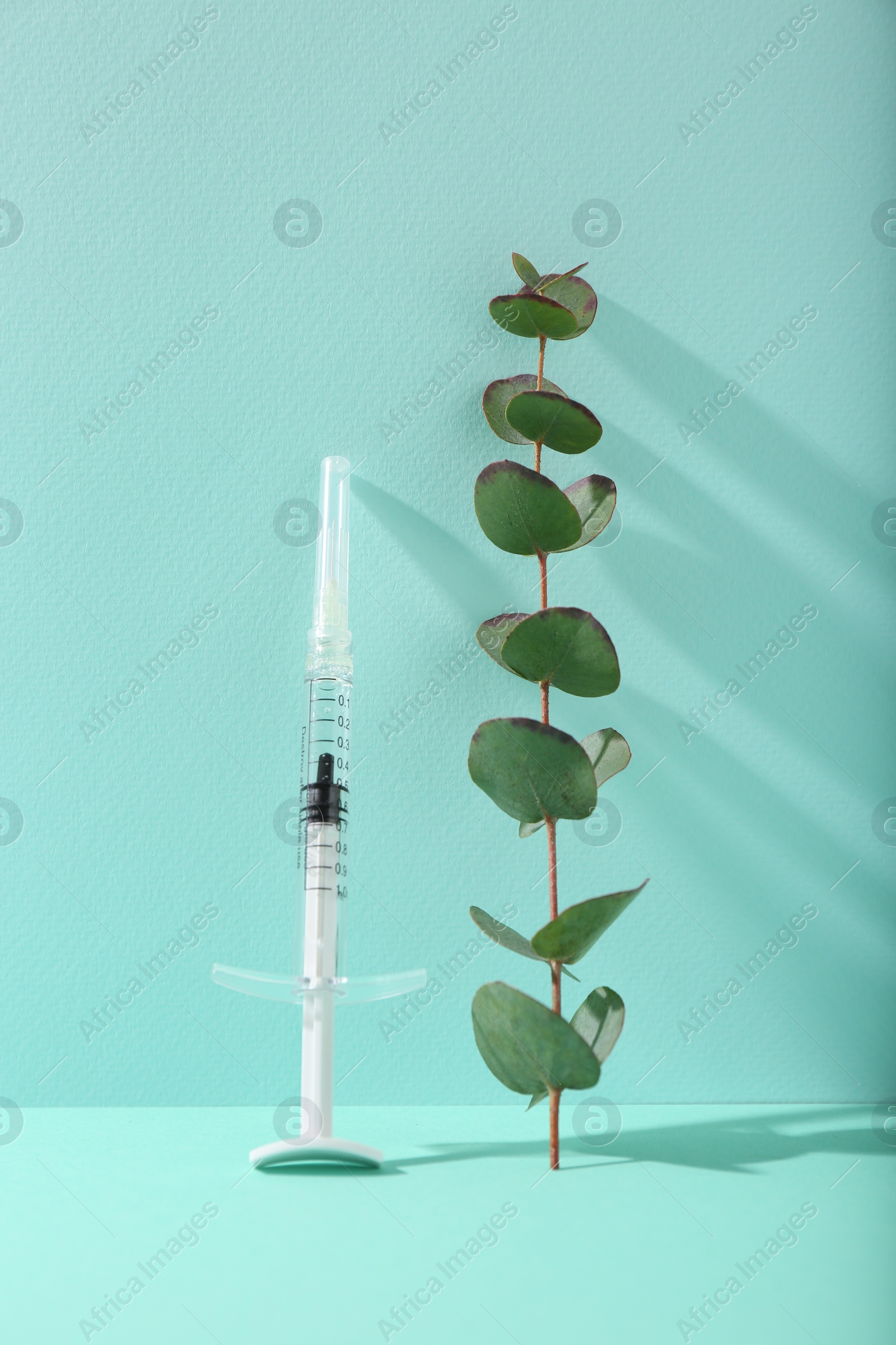 Photo of Cosmetology. Medical syringe and eucalyptus branch on turquoise background