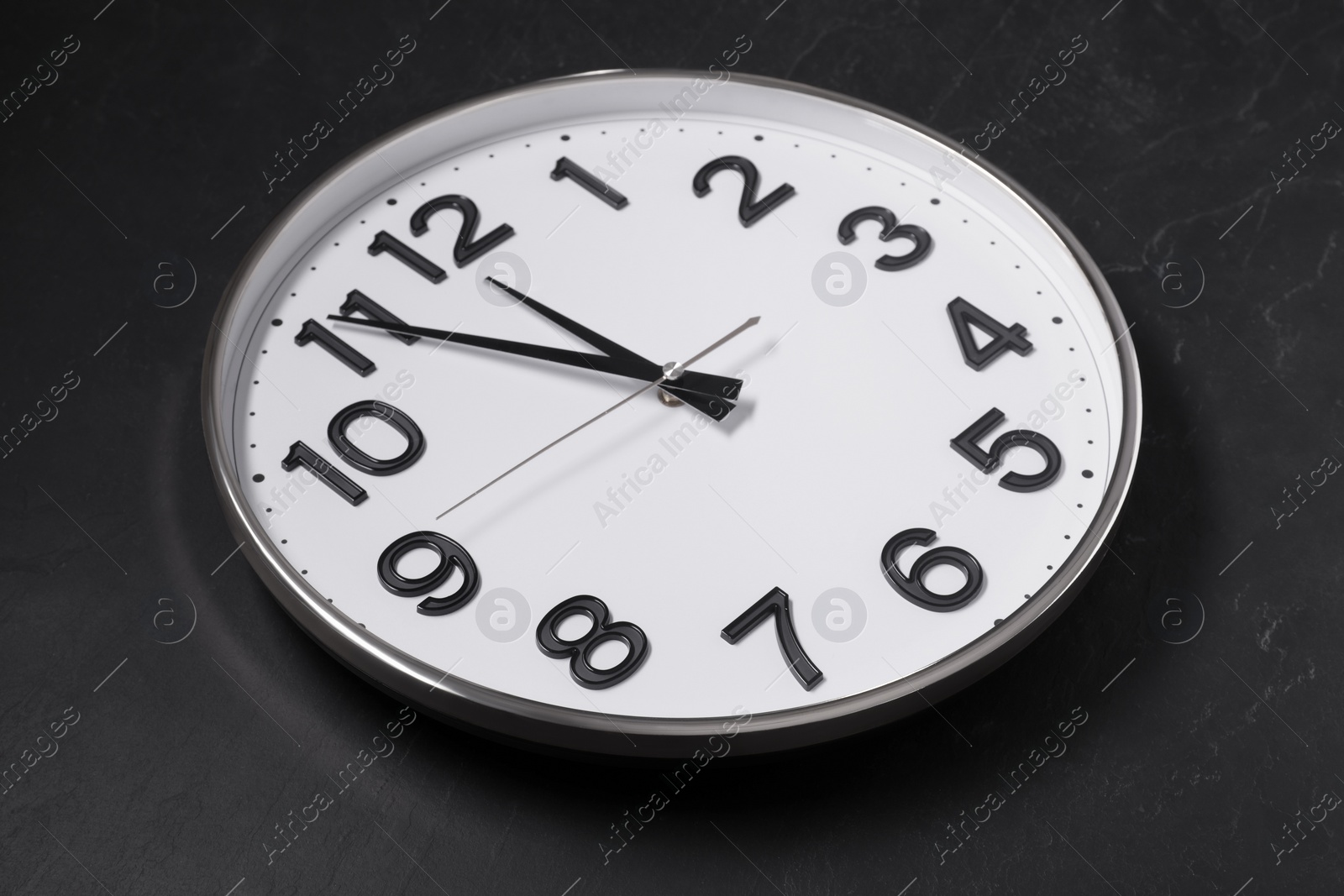 Photo of Clock showing five minutes until midnight on black table. New Year countdown