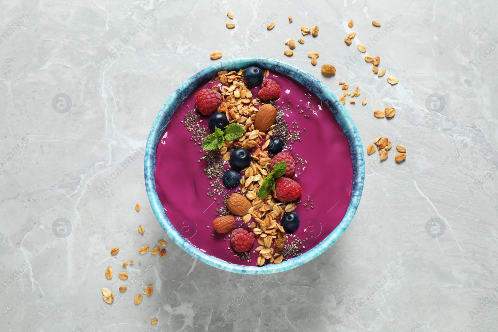 Photo of Delicious acai smoothie with granola and berries in dessert bowl on light marble table, top view