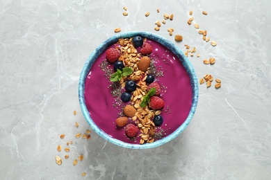 Delicious acai smoothie with granola and berries in dessert bowl on light marble table, top view