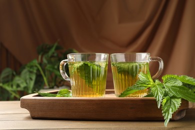 Glass cups of aromatic nettle tea and green leaves on wooden table