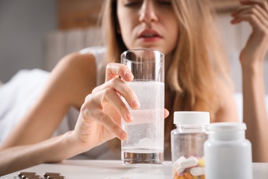 Photo of Woman taking medicine for hangover at home, focus on hand with glass