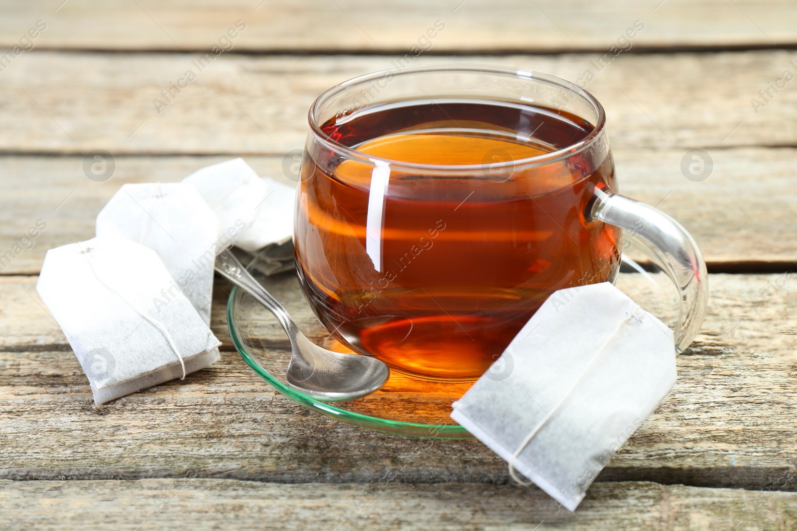 Photo of Aromatic tea in glass cup, spoon and teabags on wooden table