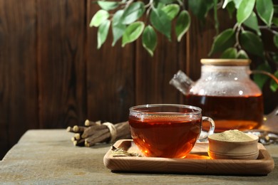 Photo of Aromatic licorice tea in cup and powder on wooden table, space for text