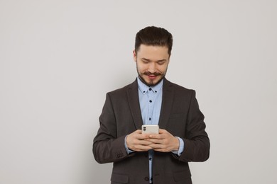 Smiling man in suit using smartphone against light grey background