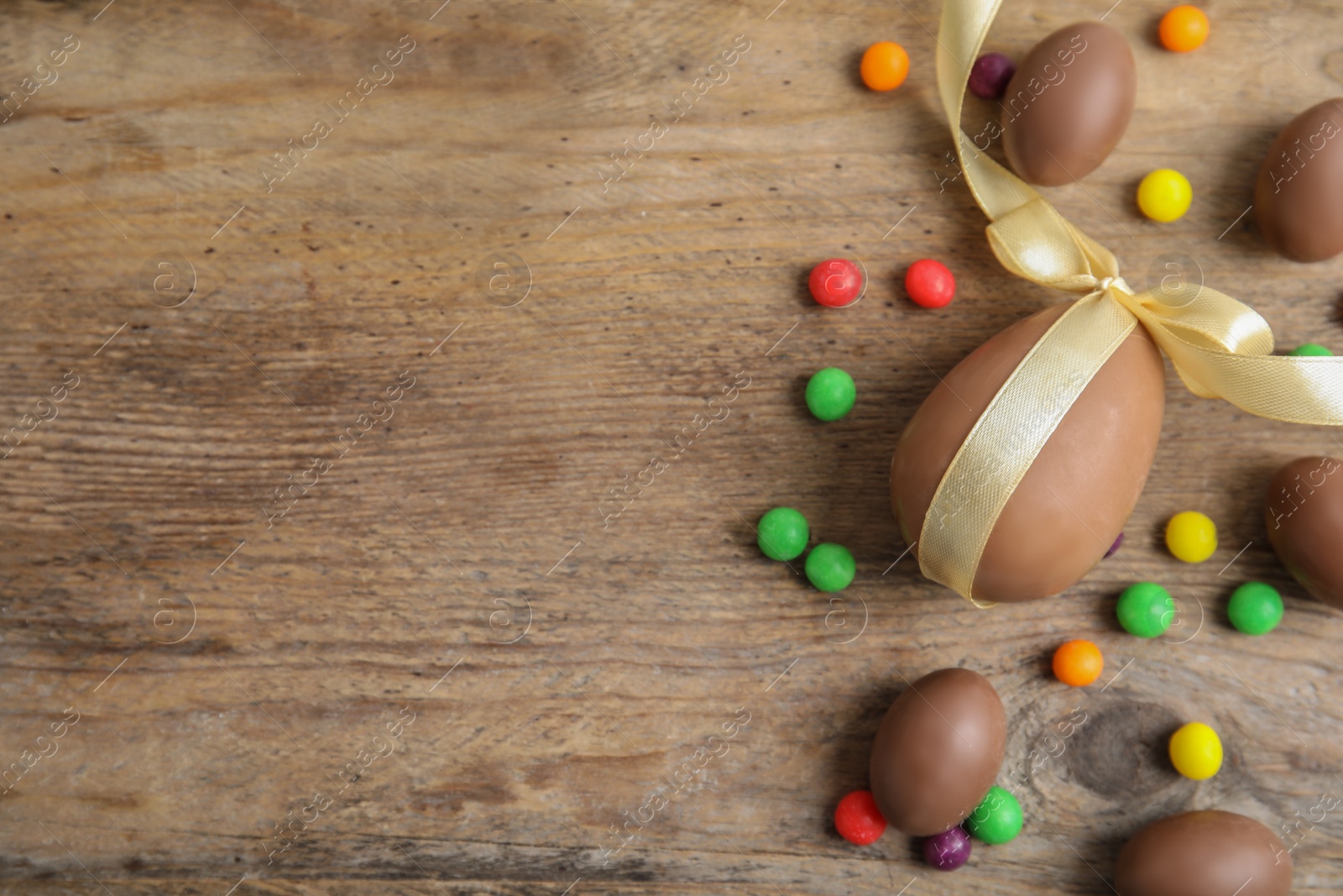 Photo of Tasty chocolate eggs and colorful candies on wooden table, flat lay. Space for text